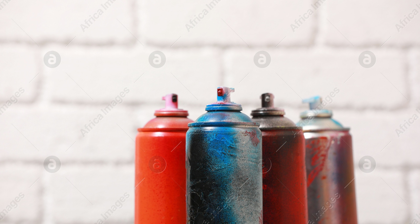 Photo of Many spray paint cans against white brick wall, closeup