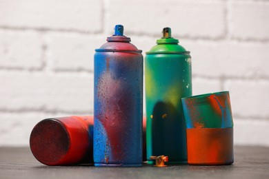 Many spray paint cans on gray surface against white brick wall