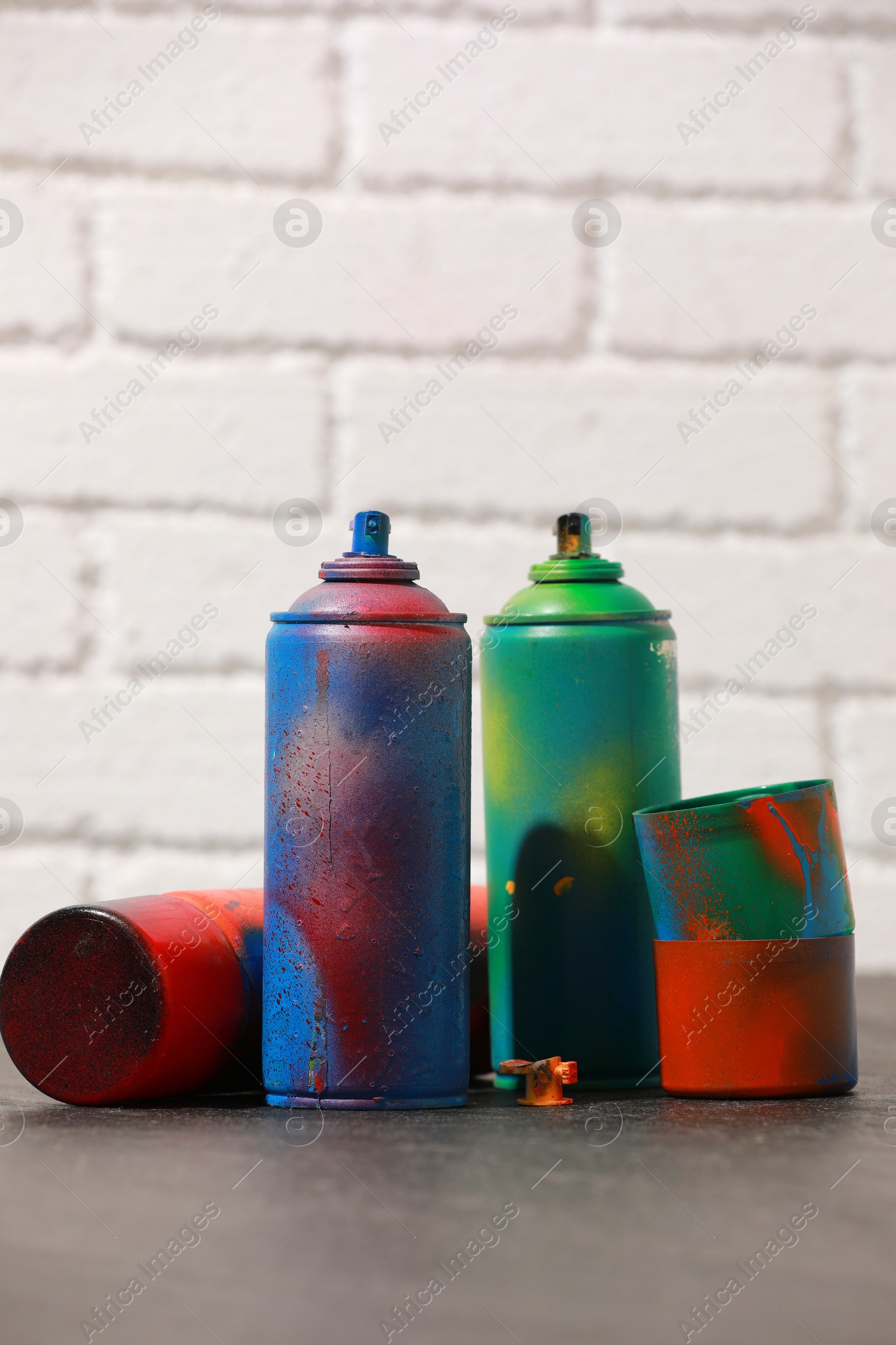 Photo of Many spray paint cans on gray surface against white brick wall