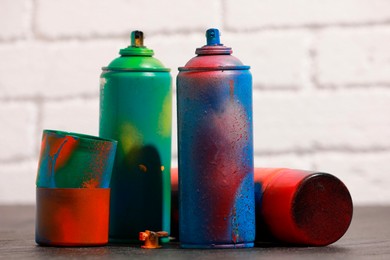 Many spray paint cans on gray surface against white brick wall