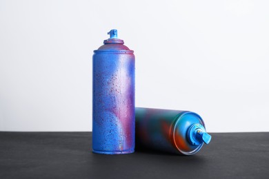 Two spray paint cans on black surface against white background