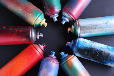 Many spray paint cans on black background, flat lay