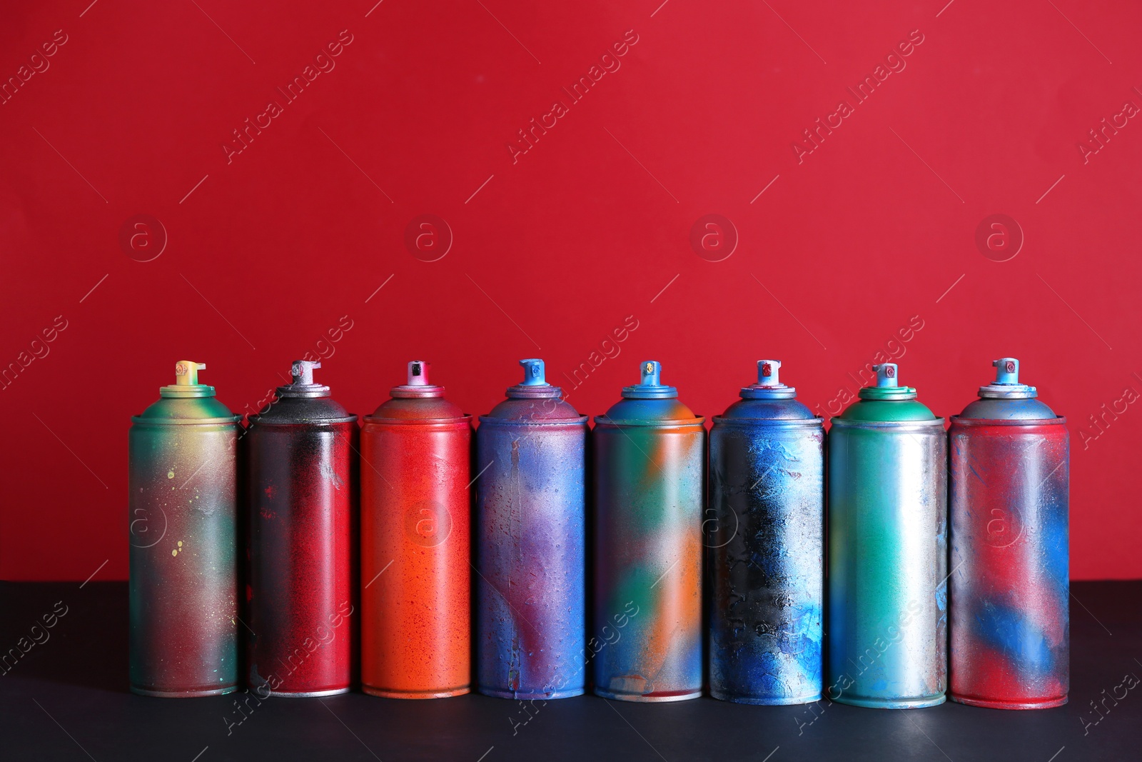 Photo of Many spray paint cans on black surface against red background, space for text