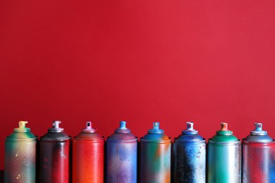 Photo of Many spray paint cans on red background, space for text