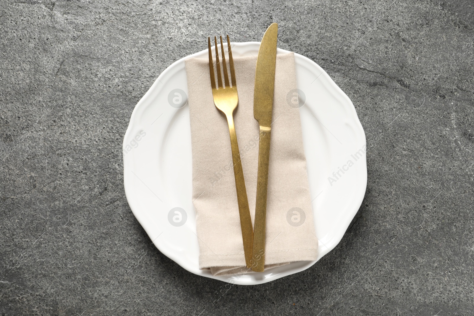 Photo of Stylish golden cutlery, plate and napkin on grey table, top view