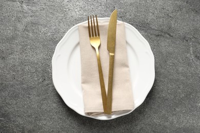 Photo of Stylish golden cutlery, plate and napkin on grey table, top view