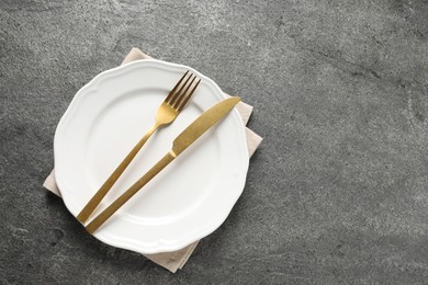 Photo of Stylish golden cutlery, plate and napkin on grey table, top view. Space for text