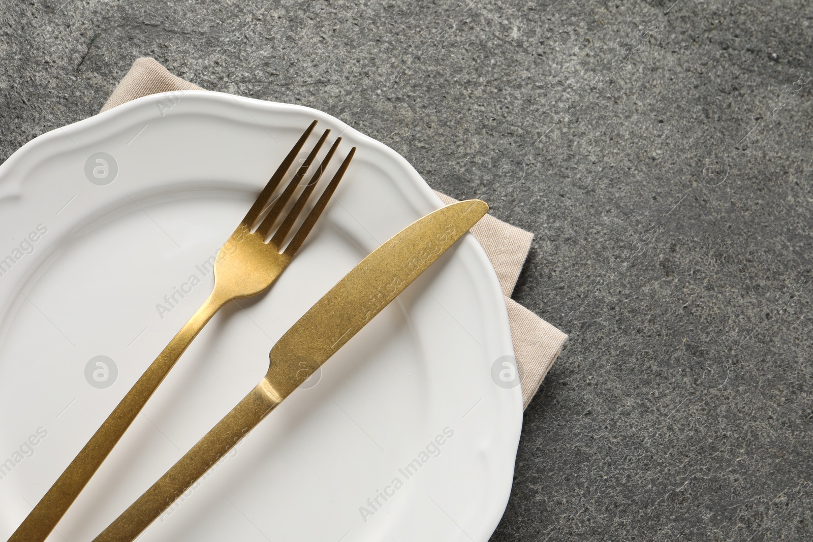 Photo of Stylish golden cutlery, plate and napkin on grey table, top view. Space for text