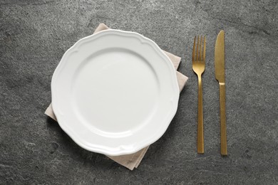 Photo of Stylish golden cutlery, plate and napkin on grey table, top view