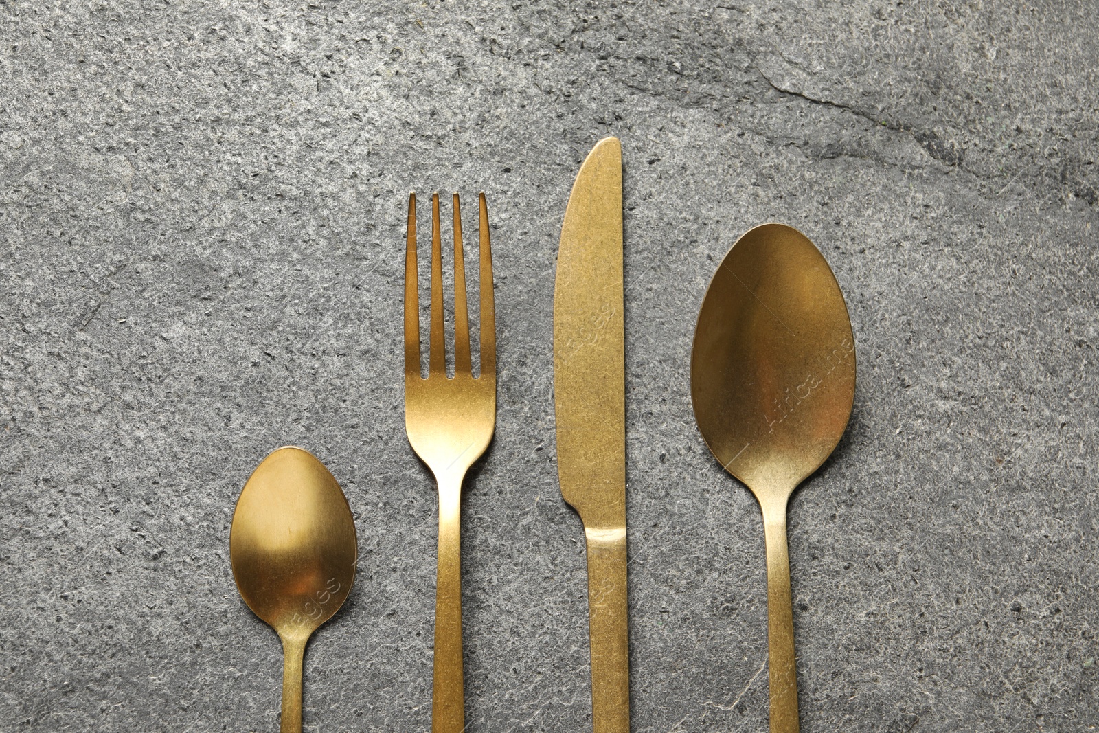 Photo of Stylish golden cutlery on grey table, flat lay