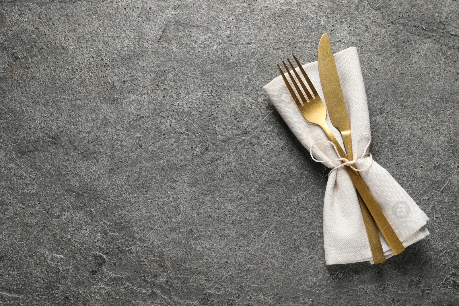 Photo of Stylish golden cutlery and napkin on grey table, top view. Space for text