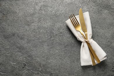 Stylish golden cutlery and napkin on grey table, top view. Space for text