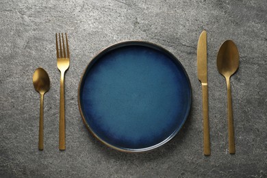 Photo of Stylish golden cutlery and plate on grey table, flat lay