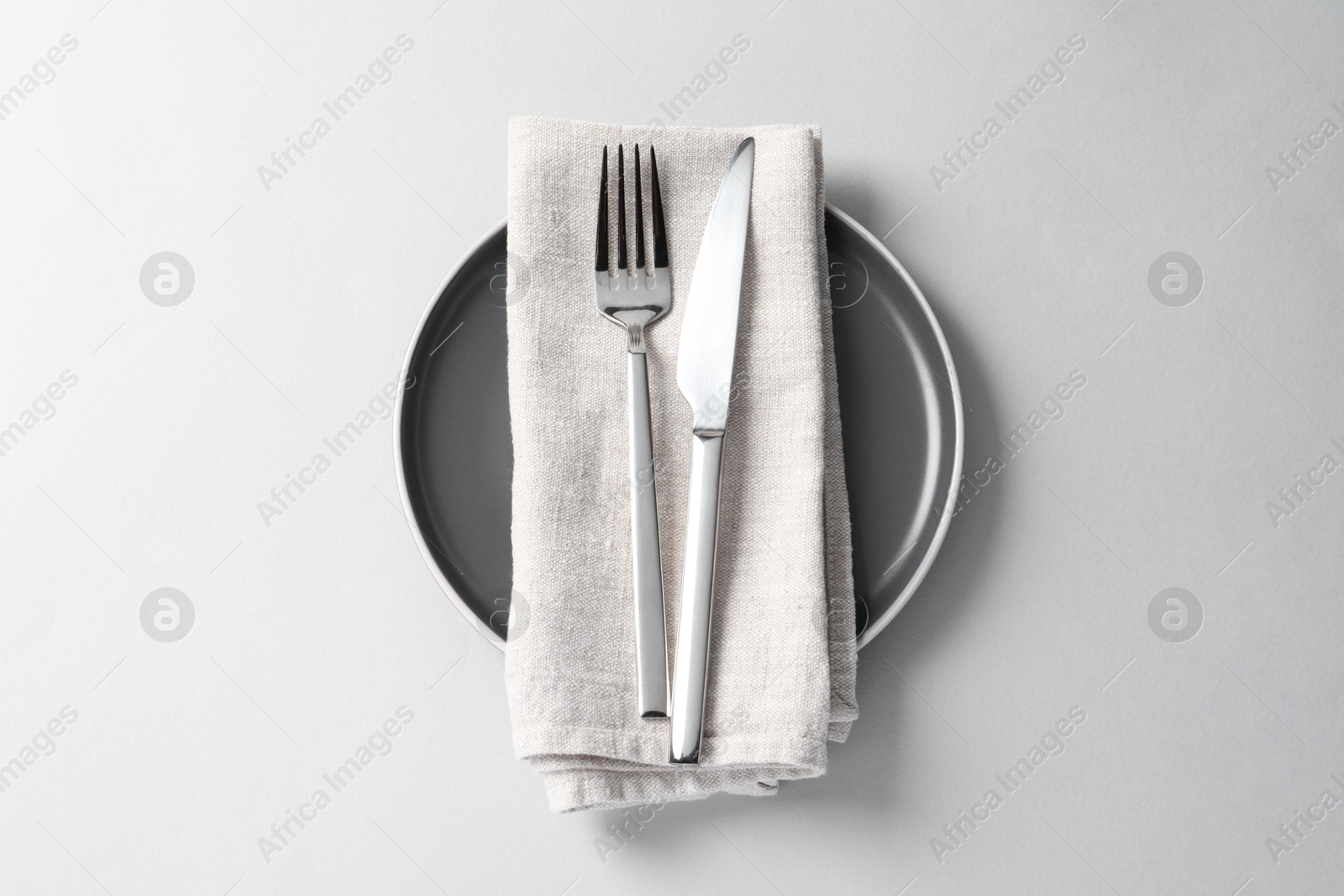 Photo of Stylish silver cutlery, plate and napkin on white background, top view