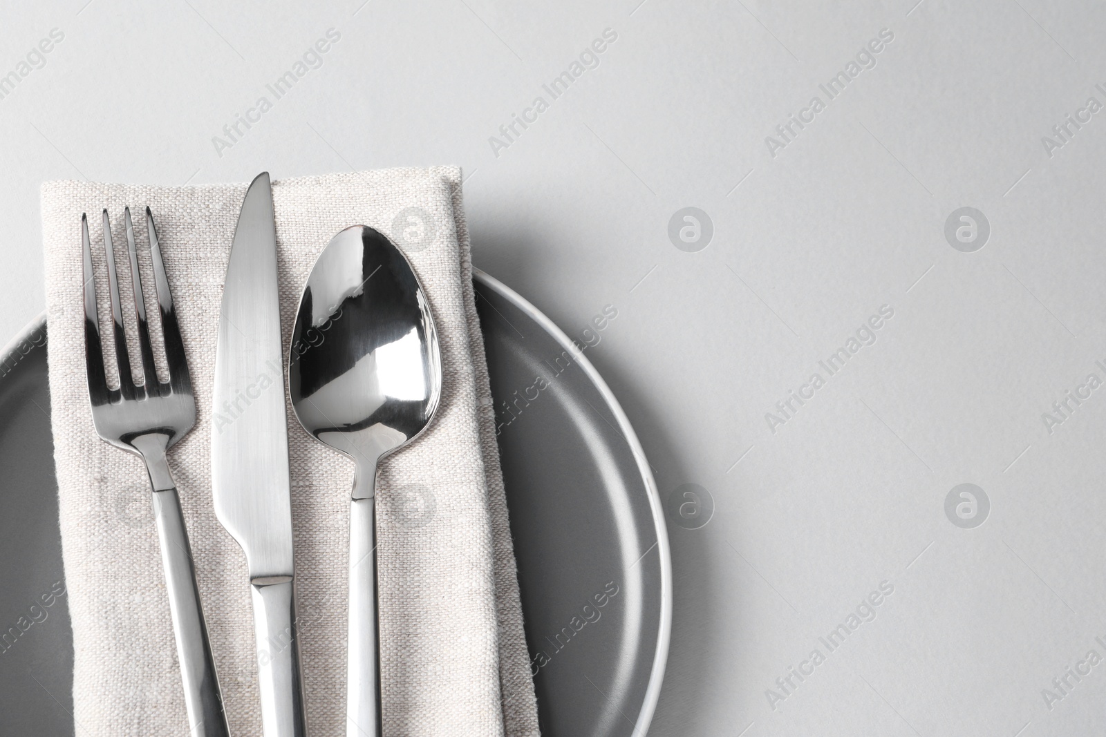 Photo of Stylish silver cutlery, plate and napkin on white background, top view. Space for text