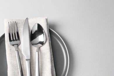 Photo of Stylish silver cutlery, plate and napkin on white background, top view. Space for text