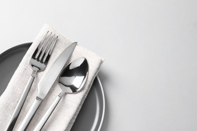 Photo of Stylish silver cutlery, plate and napkin on white background, top view. Space for text