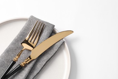 Photo of Stylish golden cutlery, plate and napkin on white background, top view. Space for text