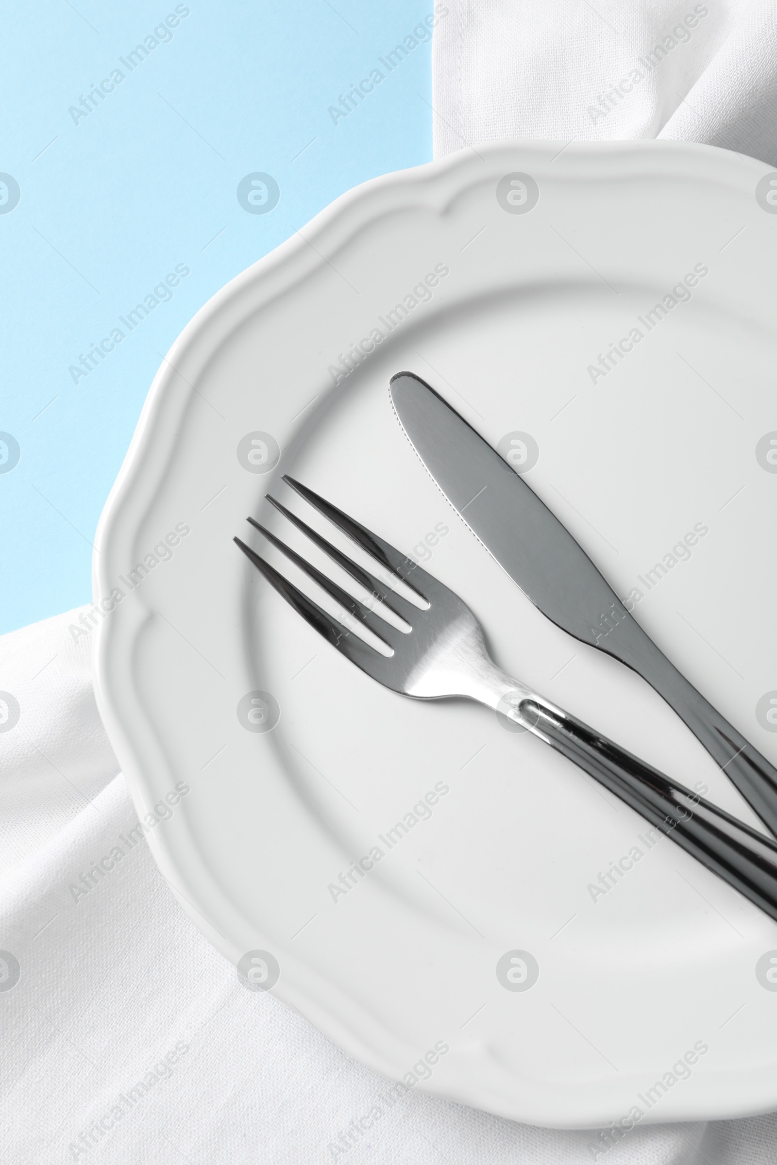 Photo of Stylish silver cutlery, plate and napkin on light blue background, top view