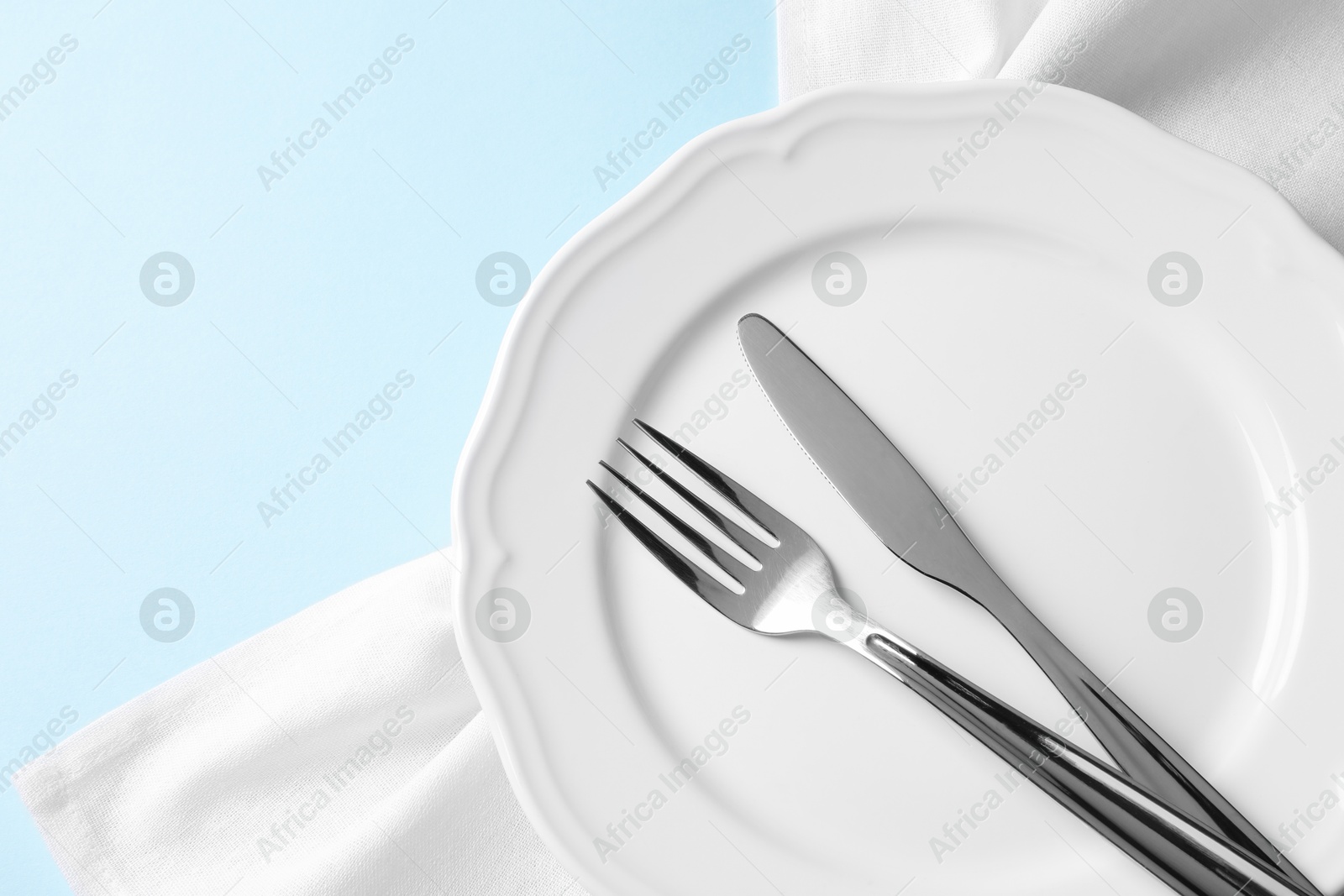 Photo of Stylish silver cutlery, plate and napkin on light blue background, top view. Space for text