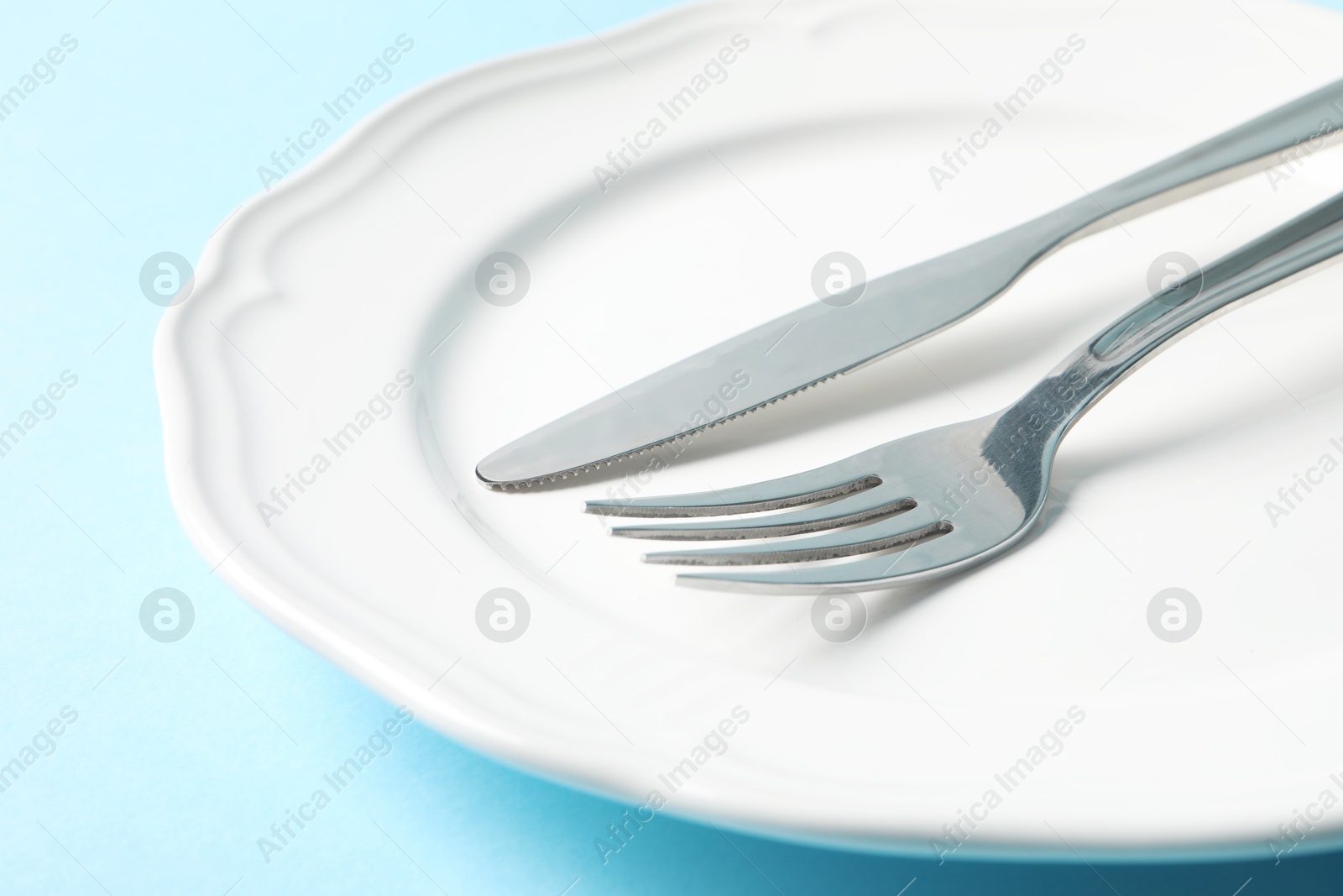 Photo of Stylish silver cutlery and plate on light blue background, closeup