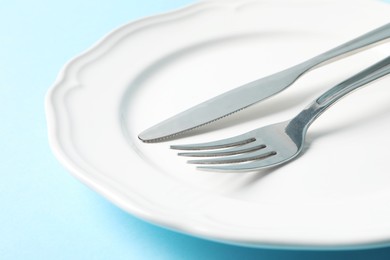 Photo of Stylish silver cutlery and plate on light blue background, closeup