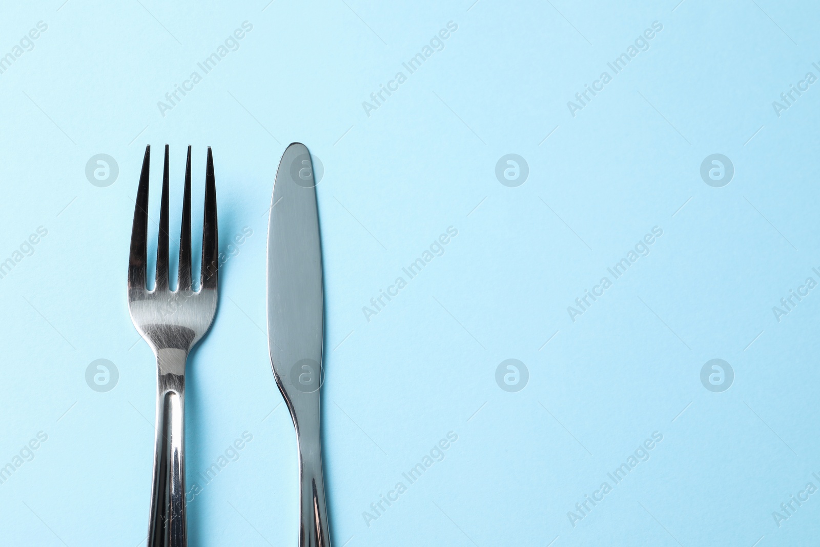 Photo of Stylish silver cutlery on light blue background, top view. Space for text