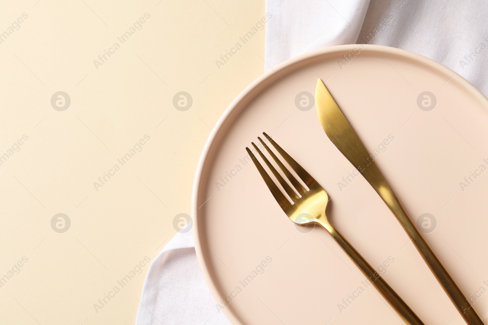 Photo of Stylish golden cutlery, plate and napkin on beige background, top view. Space for text