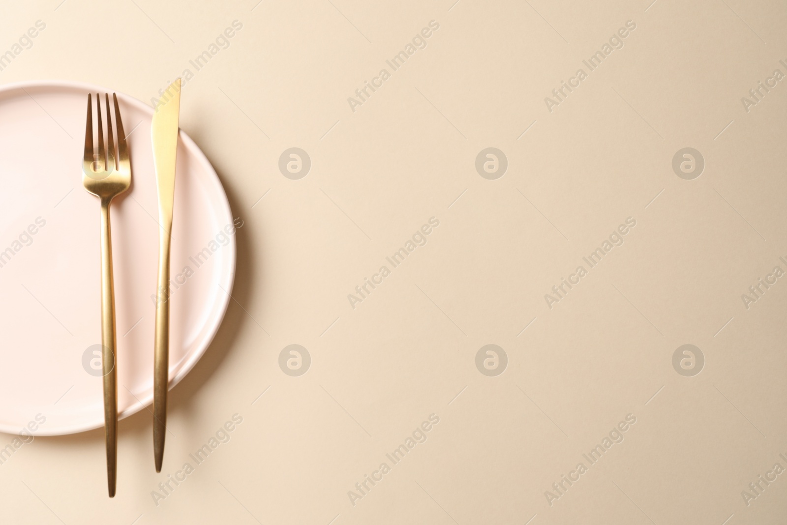 Photo of Stylish golden cutlery and plate on beige background, top view. Space for text