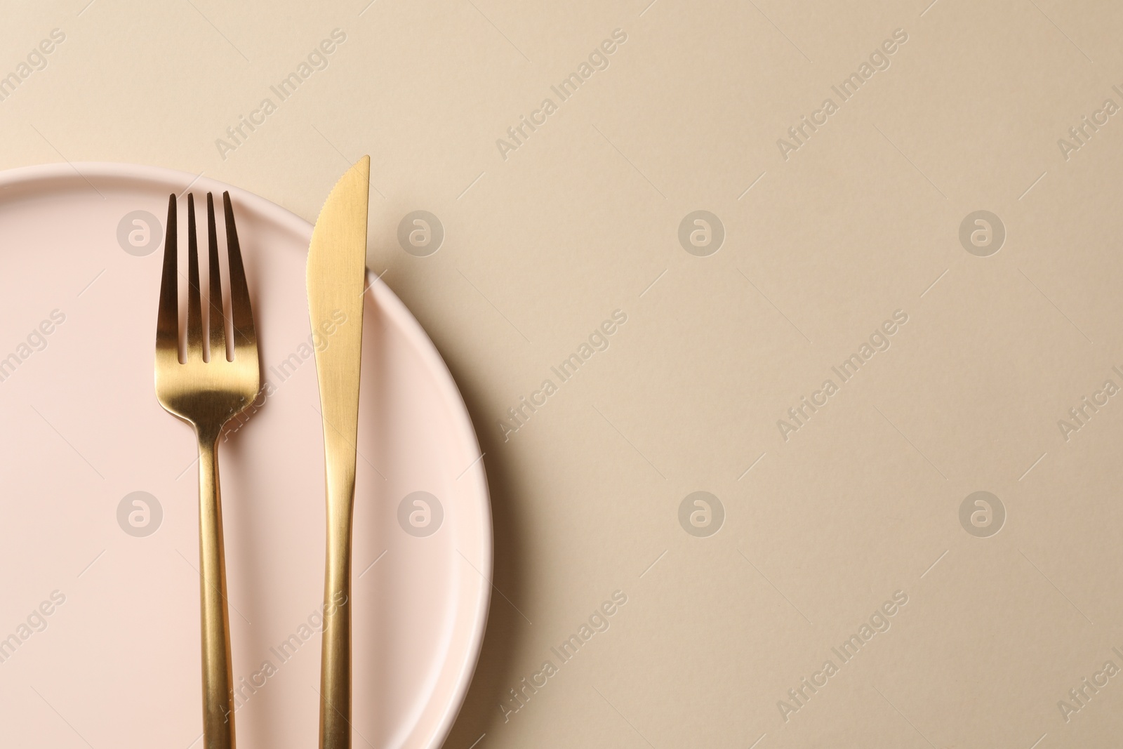 Photo of Stylish golden cutlery and plate on beige background, top view. Space for text