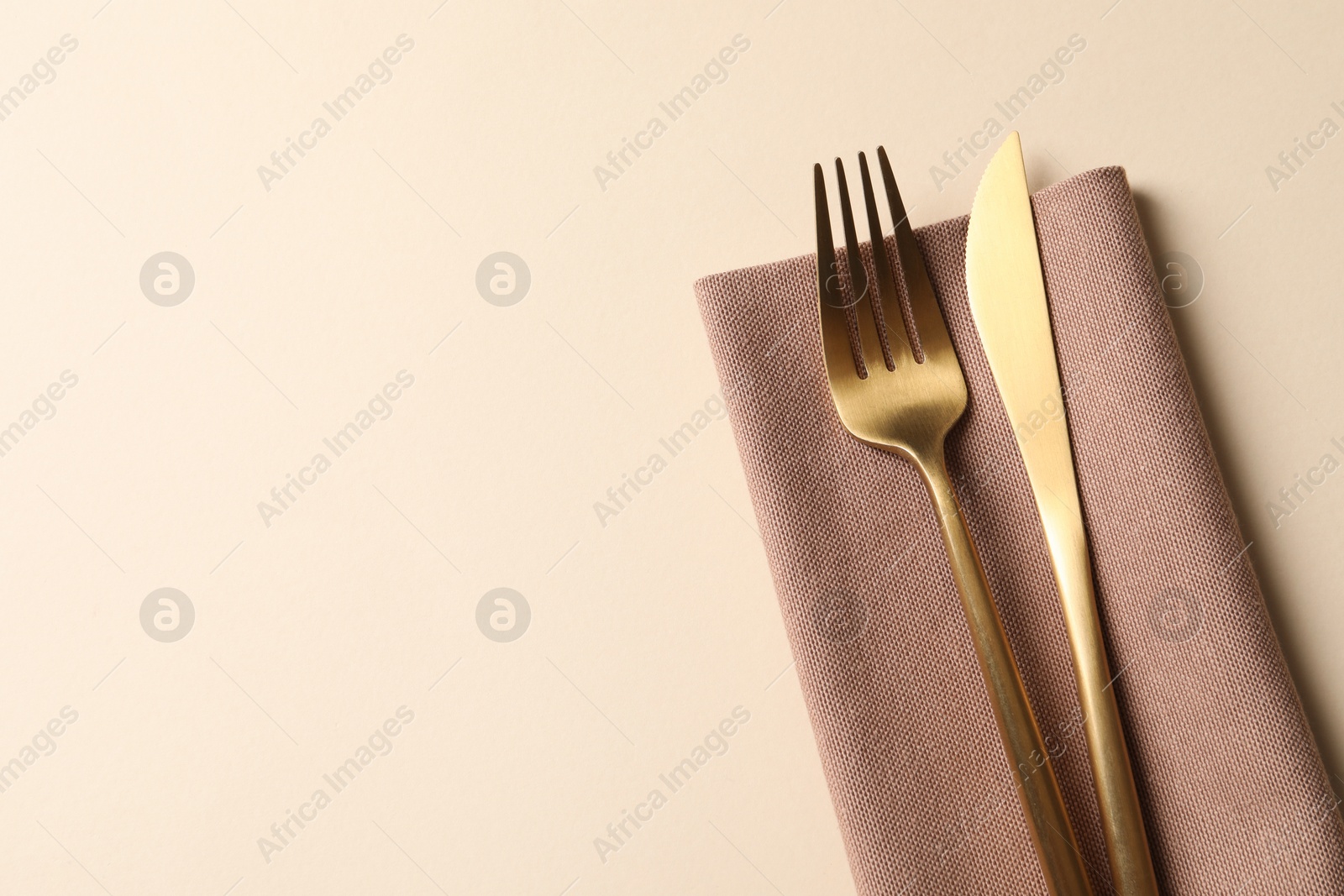 Photo of Stylish golden cutlery and napkin on beige background, top view. Space for text