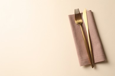 Photo of Stylish golden cutlery and napkin on beige background, top view. Space for text