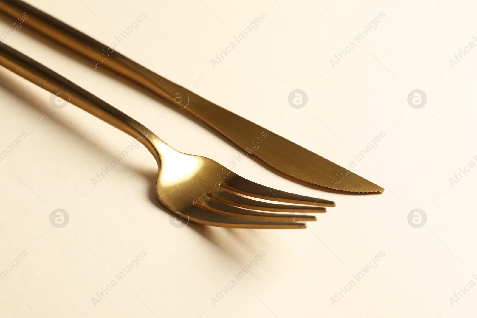 Photo of Stylish golden cutlery. Fork and knife on beige background