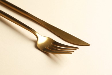 Stylish golden cutlery. Fork and knife on beige background