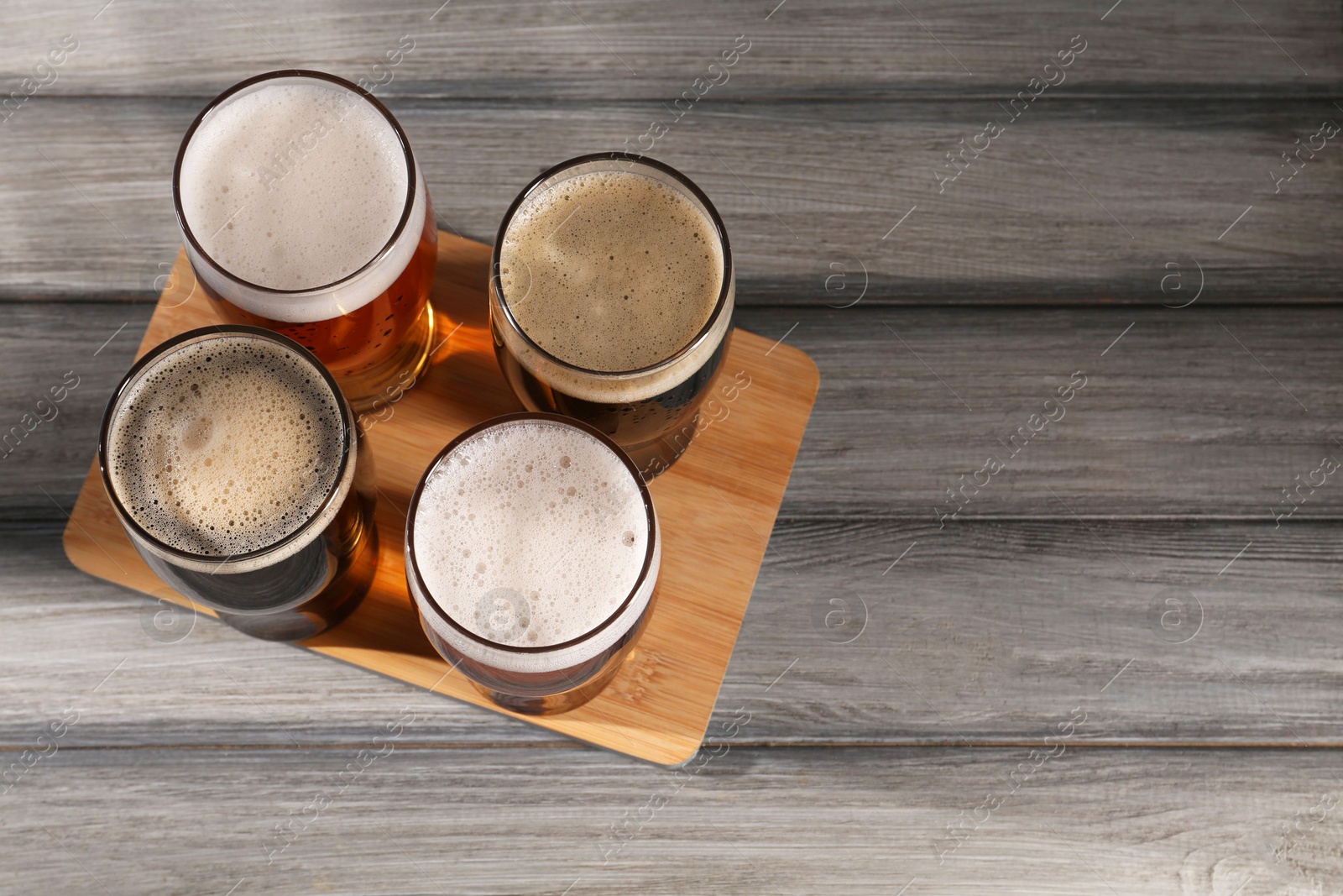 Photo of Glasses with different types of beer on grey wooden table, top view. Space for text