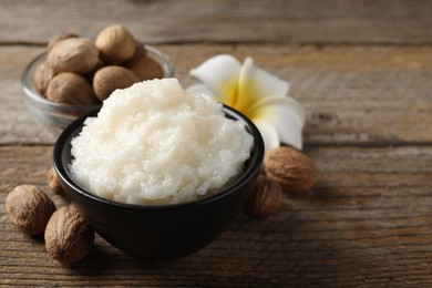 Natural shea butter in bowl, nuts and plumeria flower on wooden table, space for text