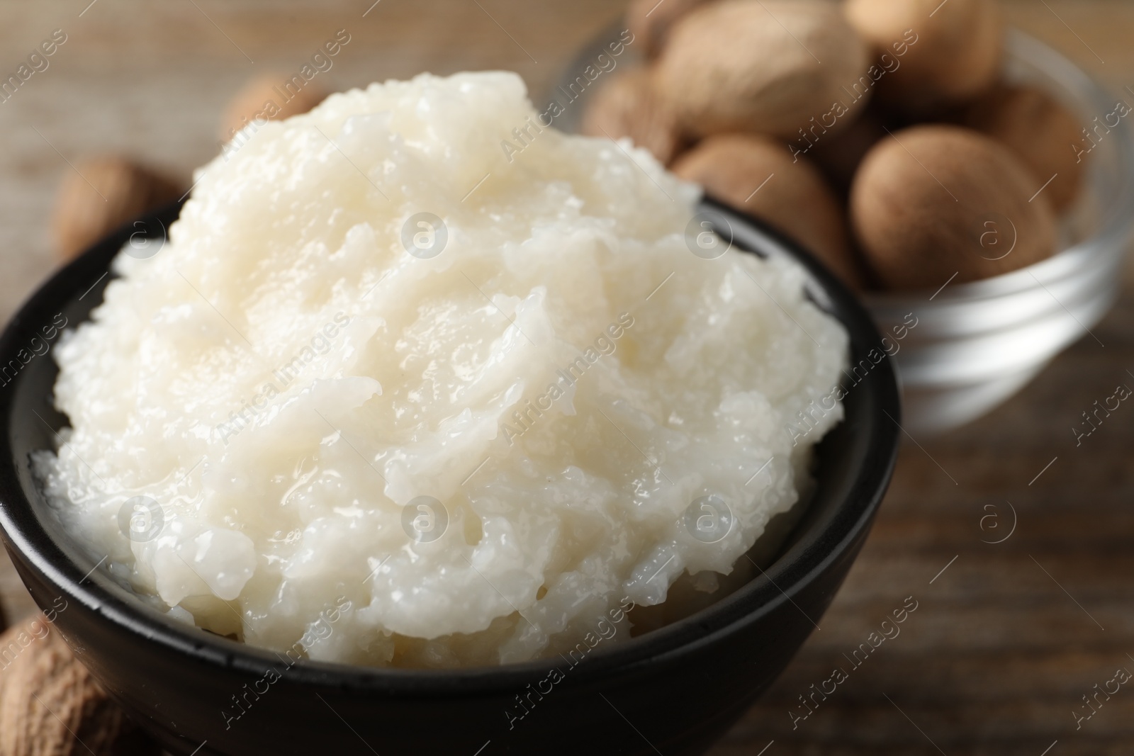 Photo of Natural shea butter in bowl and nuts on wooden table, closeup