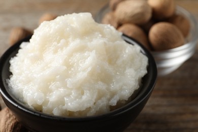 Natural shea butter in bowl and nuts on wooden table, closeup