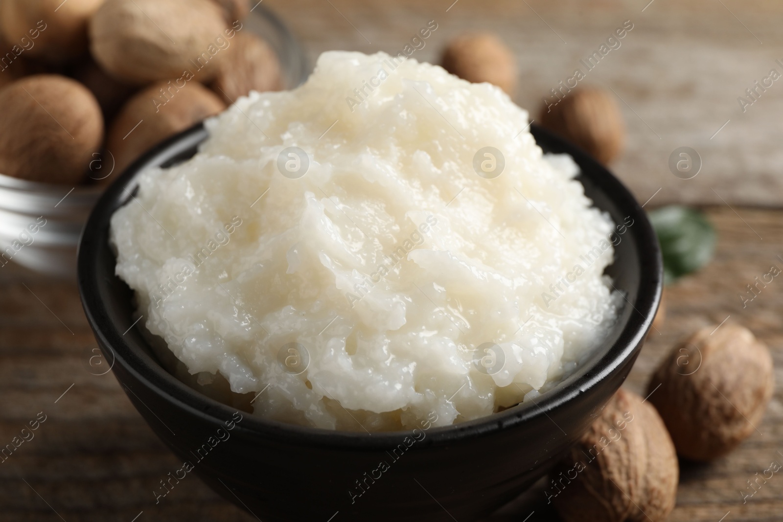 Photo of Natural shea butter in bowl and nuts on wooden table, closeup