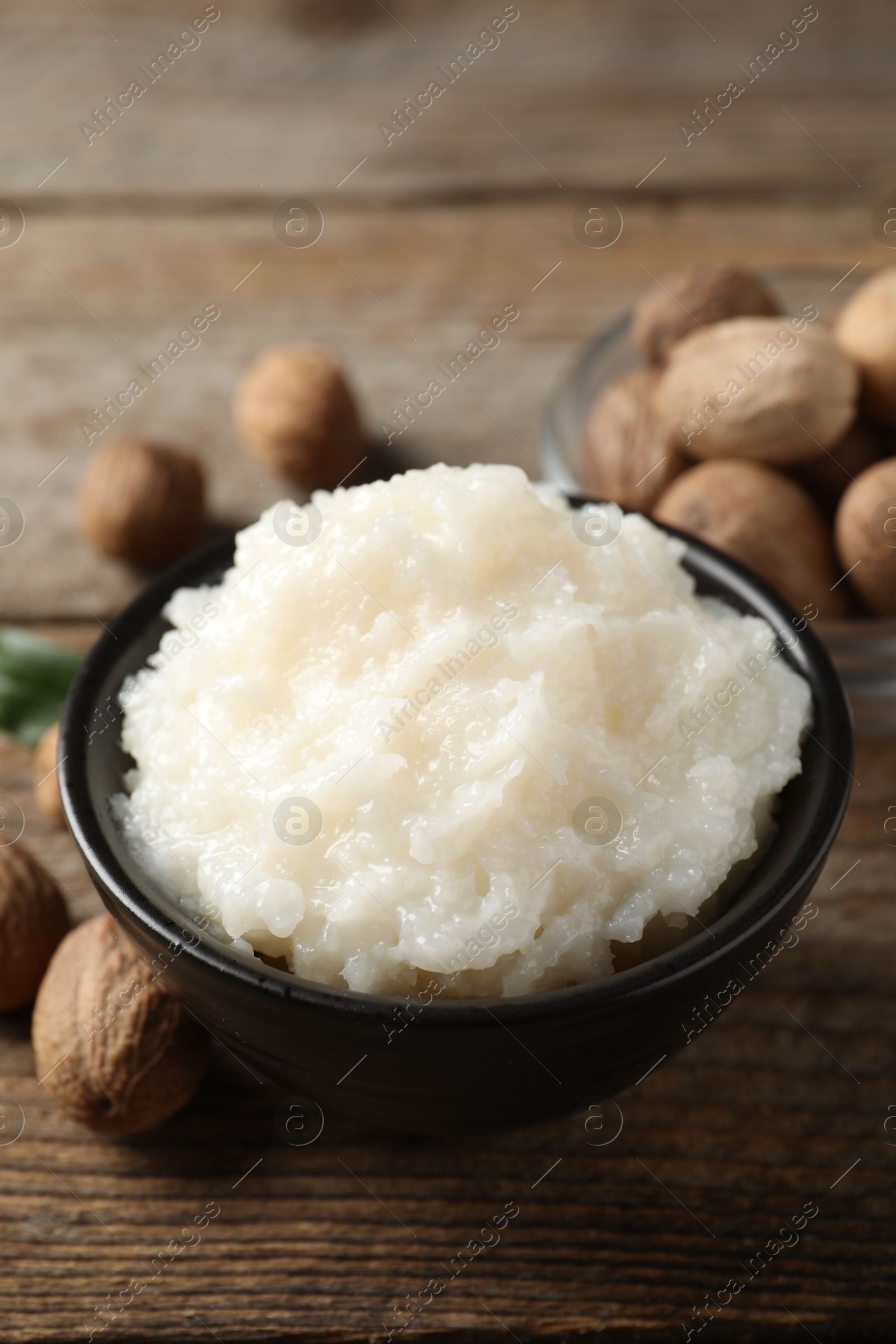 Photo of Natural shea butter in bowl and nuts on wooden table