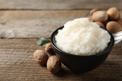 Photo of Natural shea butter in bowl and nuts on wooden table, space for text