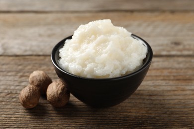 Photo of Natural shea butter in bowl and nuts on wooden table, closeup