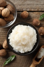 Natural shea butter in bowl and nuts on wooden table, top view