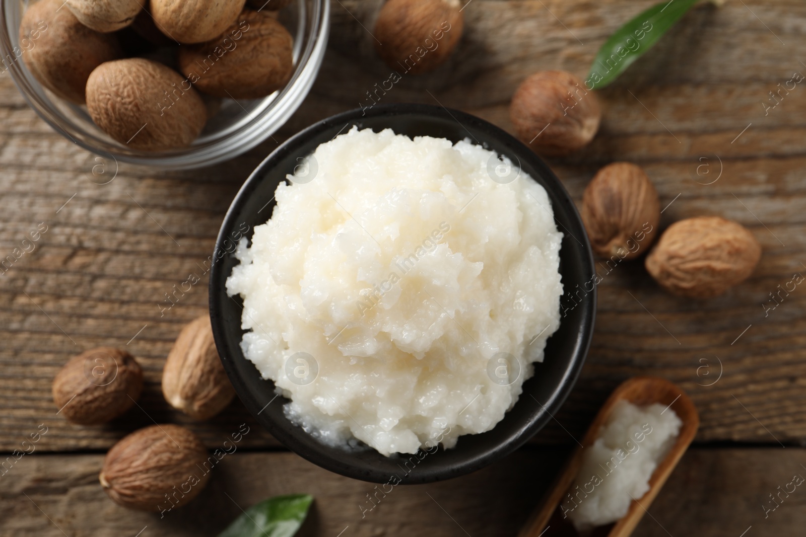 Photo of Natural shea butter in bowl and nuts on wooden table, top view