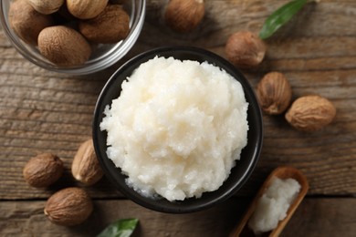 Photo of Natural shea butter in bowl and nuts on wooden table, top view