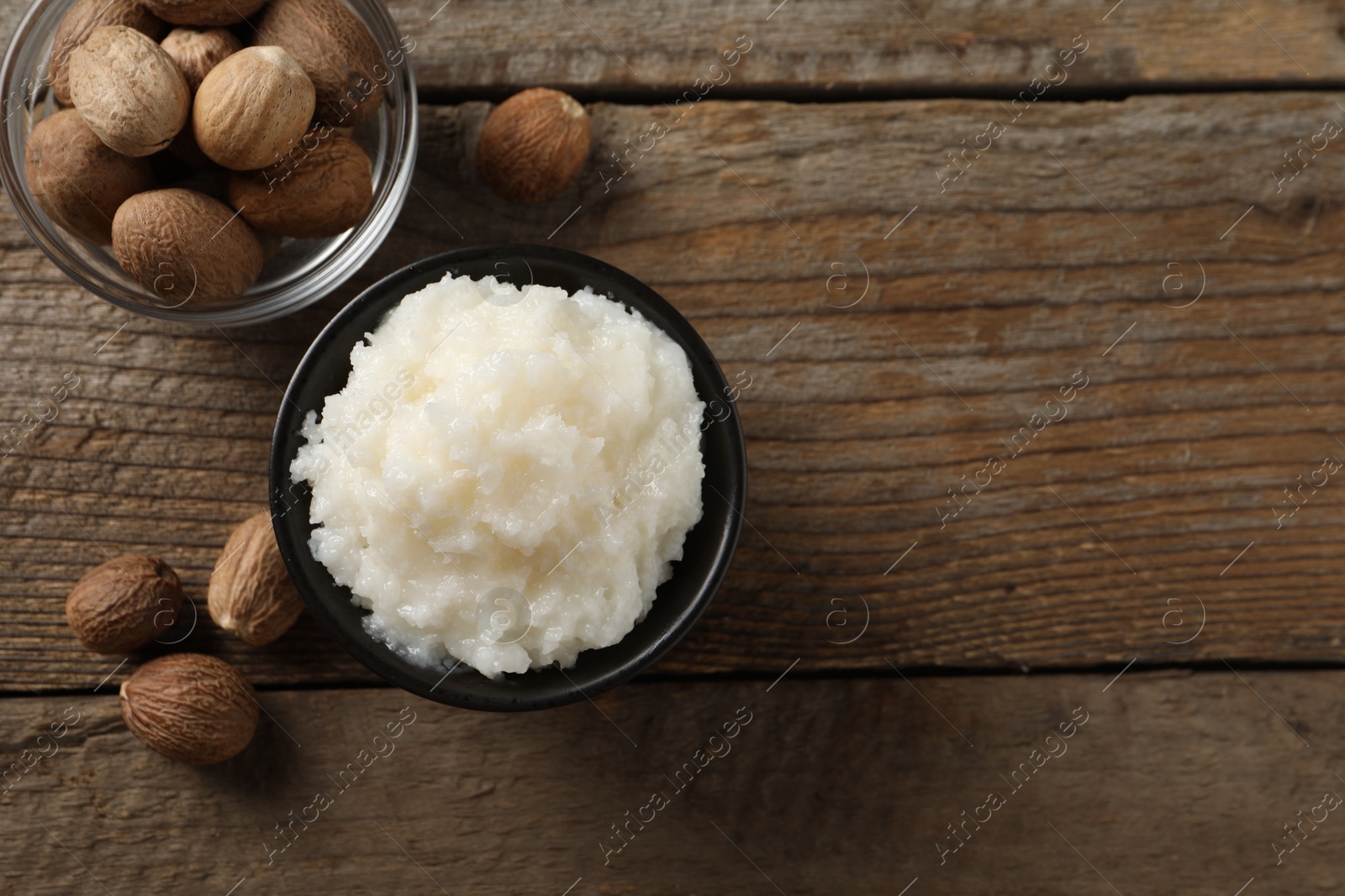 Photo of Natural shea butter in bowl and nuts on wooden table, top view. Space for text