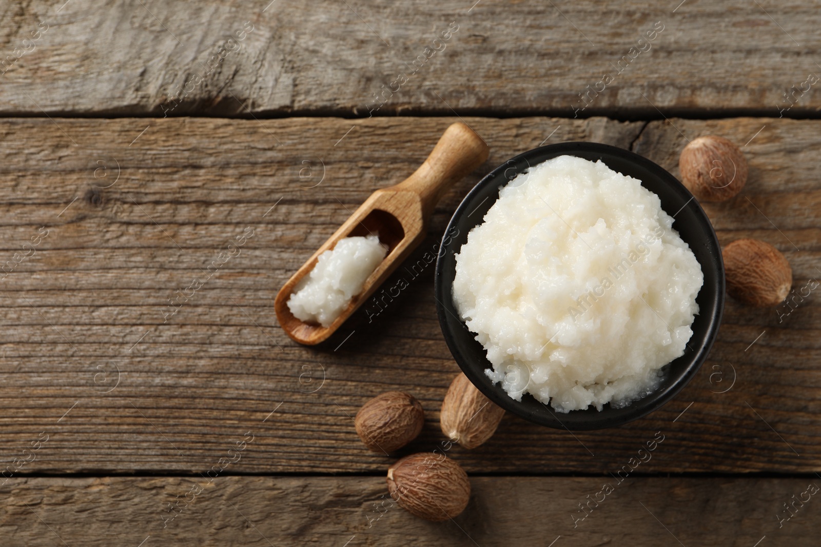 Photo of Natural shea butter in bowl and nuts on wooden table, top view. Space for text