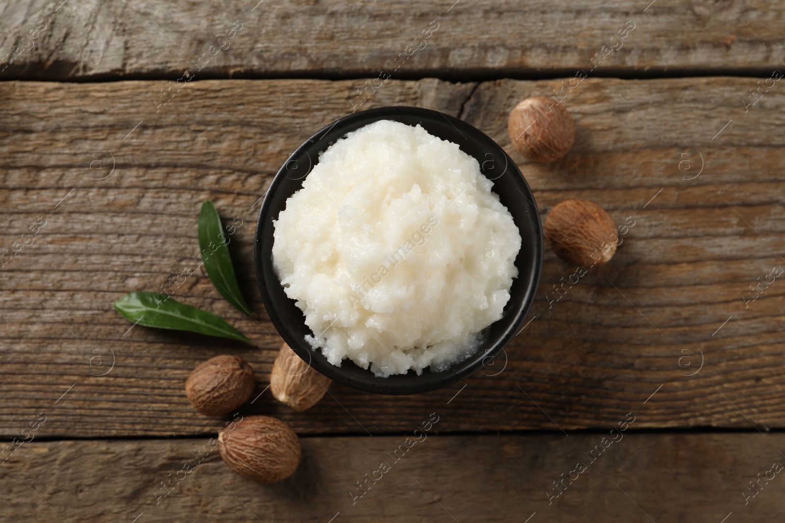 Photo of Natural shea butter in bowl and nuts on wooden table, top view