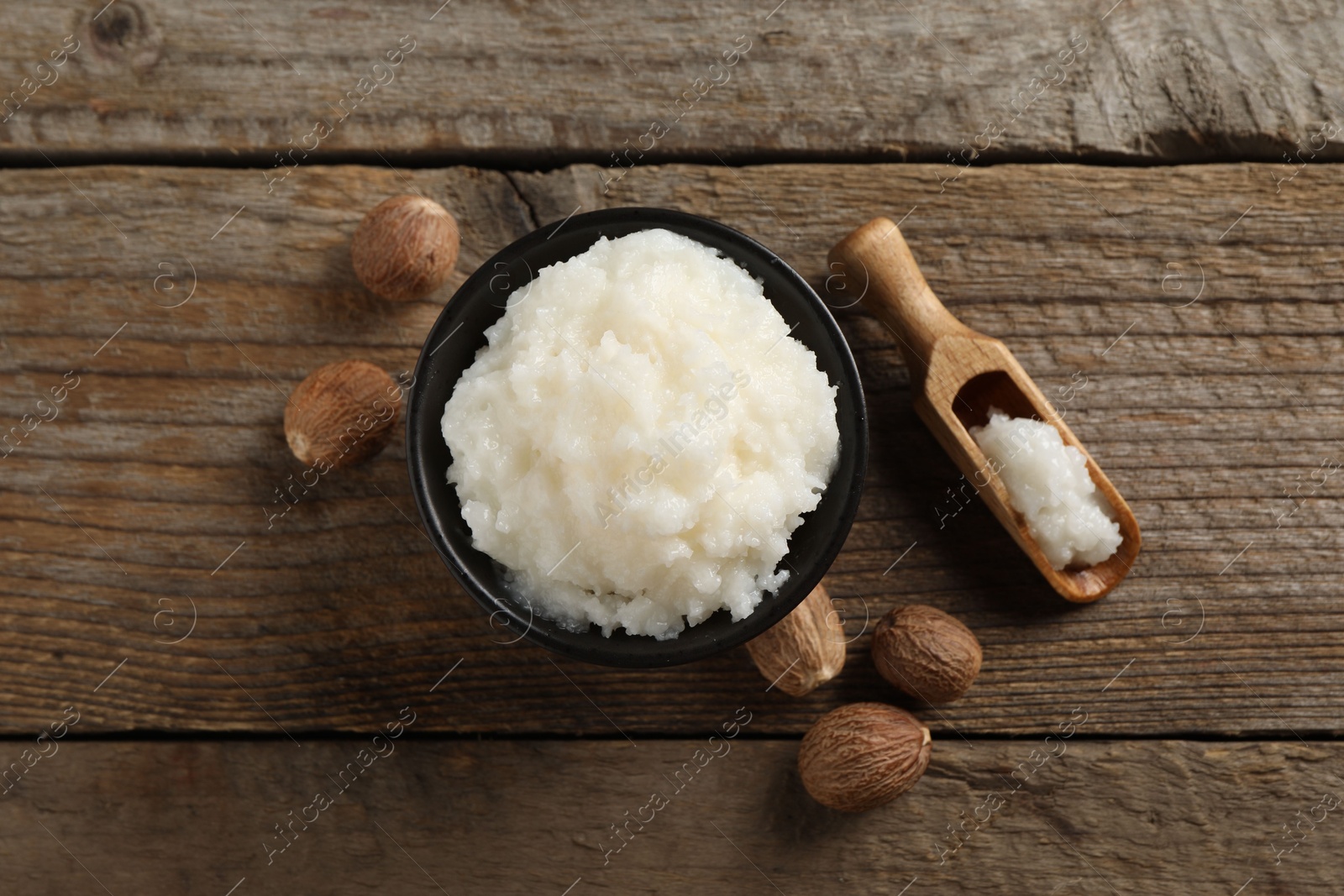 Photo of Natural shea butter in bowl and nuts on wooden table, top view