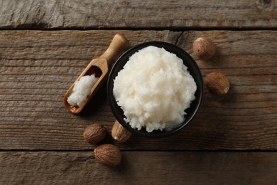 Photo of Natural shea butter in bowl and nuts on wooden table, top view